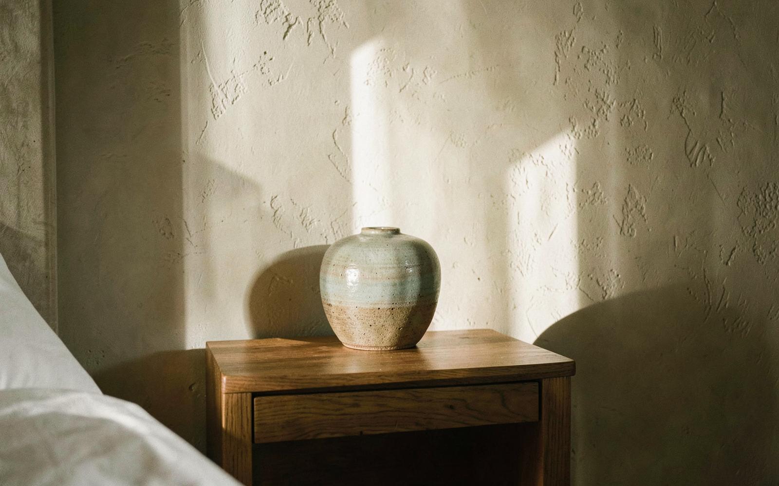 Handgemachte Keramikvase auf einem Holznachttisch vor verputzter Wand